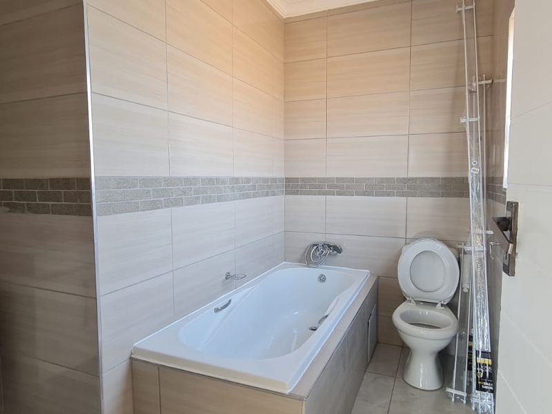 A clean, modern bathroom featuring neutral wall tiles, a built-in bathtub, a vanity with a basin, and a standard toilet.