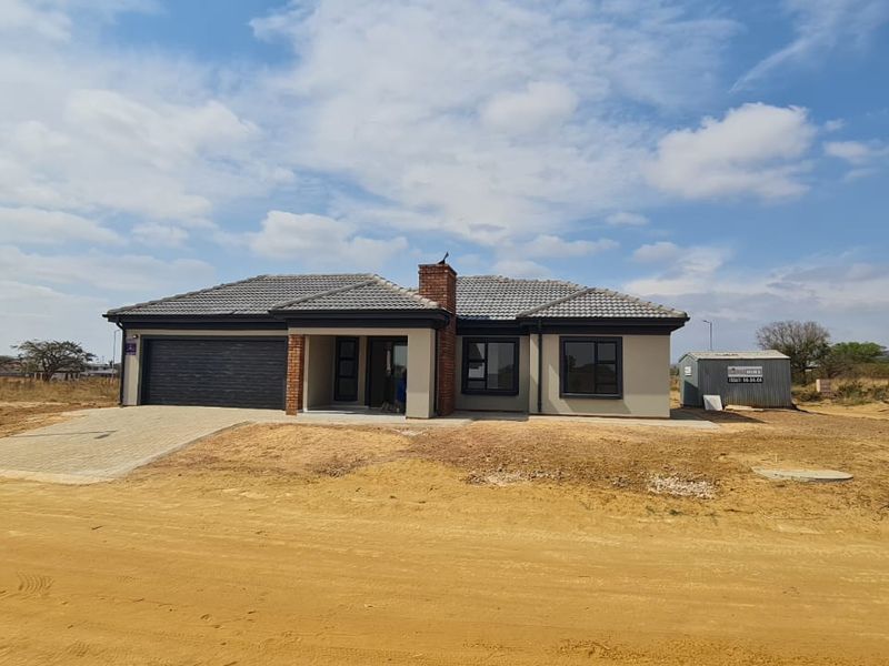 A modern single-story residential home featuring a tiled roof, brick chimney, paved driveway, and integrated garage, situated on an undeveloped plot.