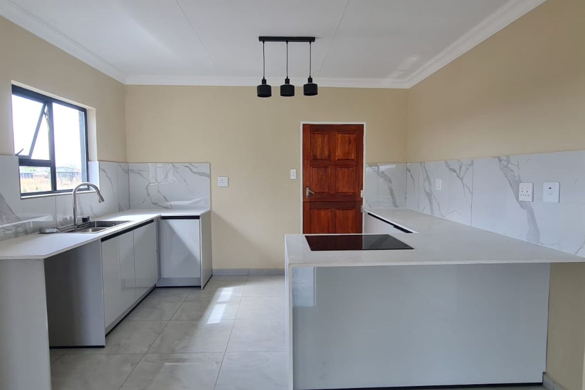 A modern, clean kitchen featuring white cabinetry, marble-look splashbacks, quartz countertops, and a built-in hob, finished with contemporary pendant lighting and tiled floors.