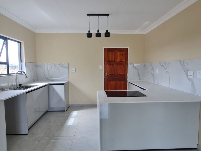 A modern, clean kitchen featuring white cabinetry, marble-look splashbacks, quartz countertops, and a built-in hob, finished with contemporary pendant lighting and tiled floors.