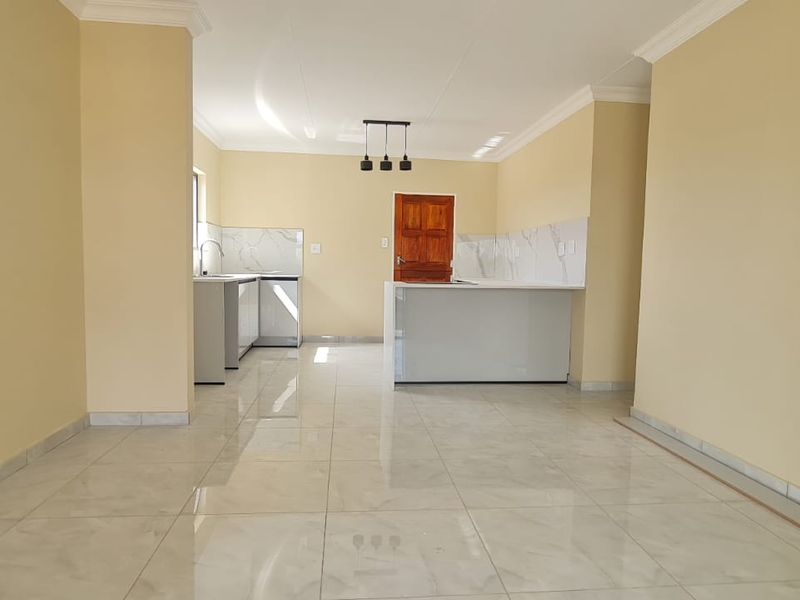 A bright, open-plan living and kitchen area featuring modern tiled flooring, a central kitchen island, and clean, neutral wall finishes.