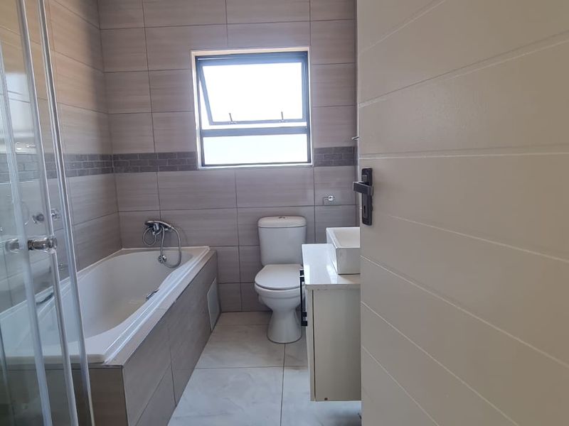 A modern, well-maintained bathroom featuring a bathtub, separate shower enclosure, toilet, and a vanity basin with neutral wall and floor tiling.