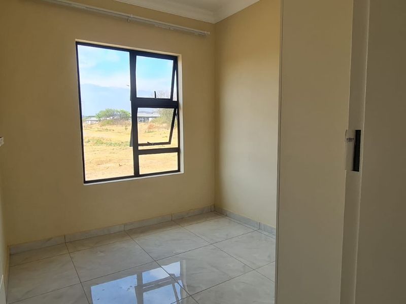 A clean, empty bedroom featuring tiled flooring, a built-in wardrobe, and a large window providing natural light.
