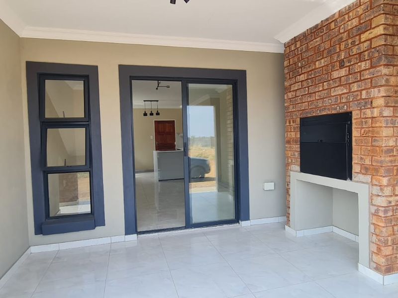 Covered patio featuring tiled flooring, a built-in braai with exposed brickwork, and sliding glass doors providing access to the interior living space.