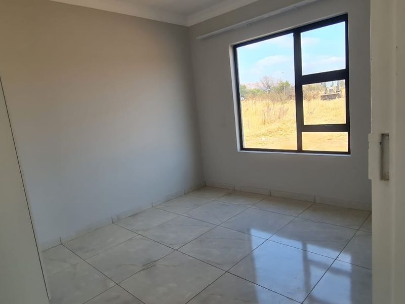 A clean, empty bedroom featuring neutral tiled flooring, a built-in cupboard, and a large aluminium-framed window providing natural light.
