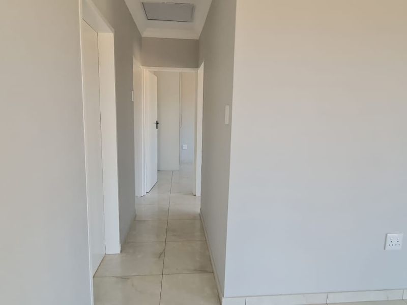 A clean, neutral-toned hallway featuring tiled flooring and access to multiple internal rooms, presenting a well-maintained and functional transition space.