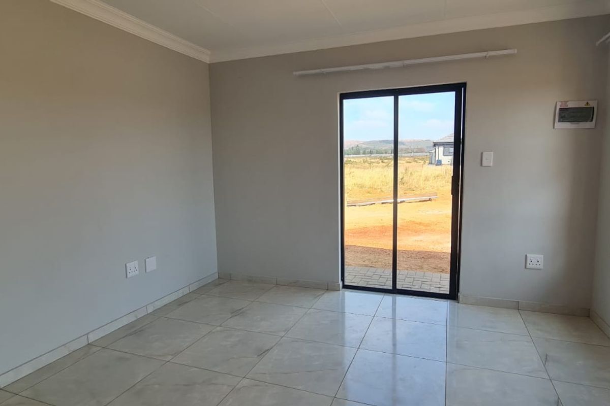 A bright, empty living area featuring neutral tiled flooring, modern aluminium window frames, and a sliding glass door leading to the exterior.