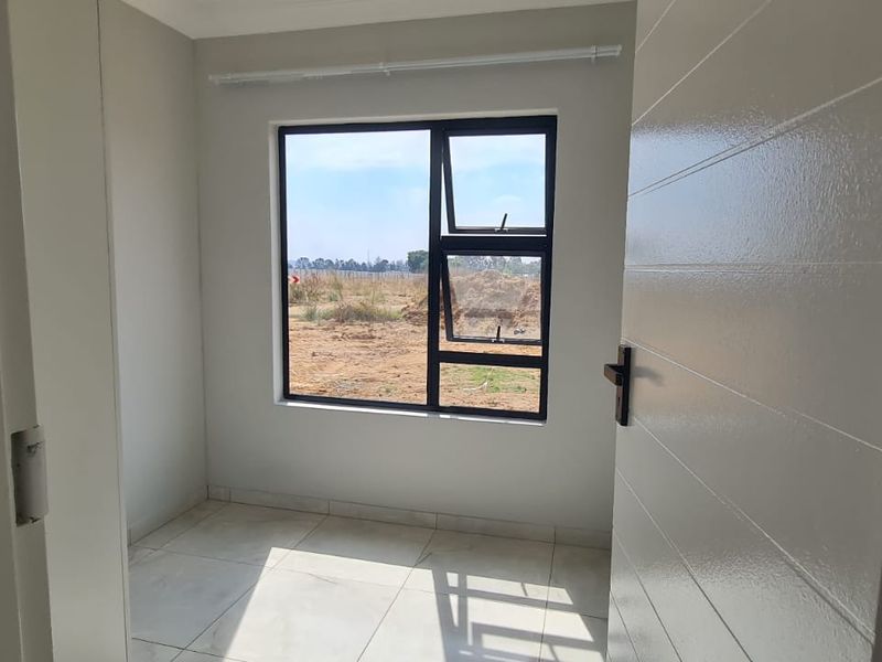 A bright, empty bedroom featuring neutral tiled flooring and a modern aluminium window frame, offering a clean and versatile space ready for personalization.
