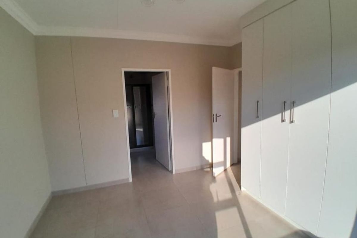 A clean, empty bedroom featuring neutral tiled flooring, built-in cupboards, and crisp white finishes, offering a versatile space ready for personalization.