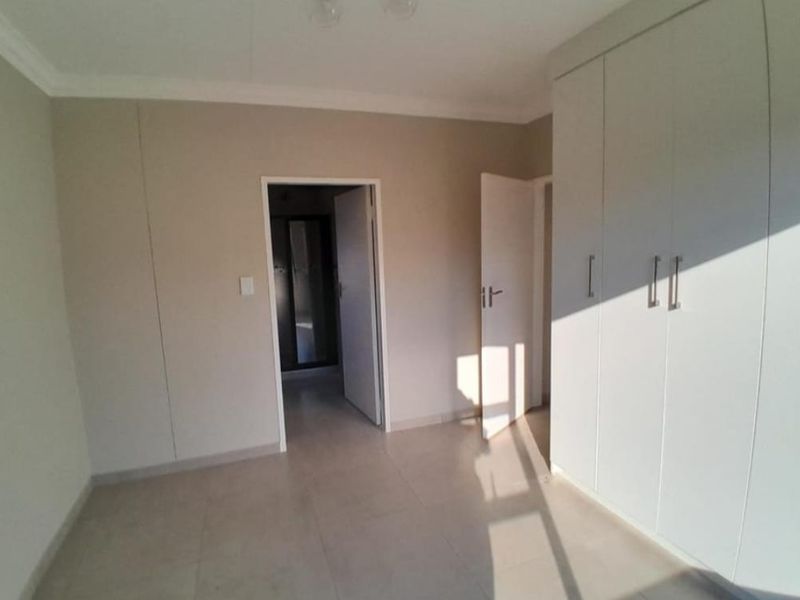 A clean, empty bedroom featuring neutral tiled flooring, built-in cupboards, and crisp white finishes, offering a versatile space ready for personalization.