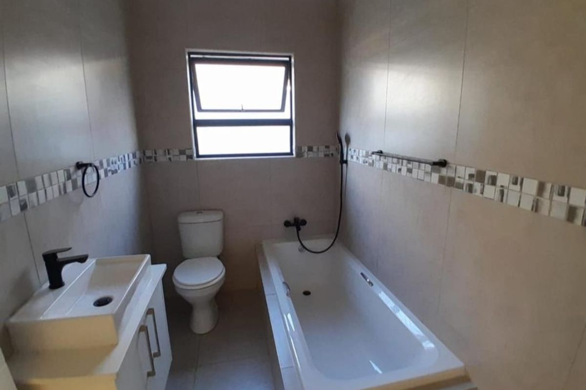 A clean, modern bathroom featuring a built-in bathtub, a contemporary vanity with basin, and a toilet, finished with neutral wall and floor tiles.