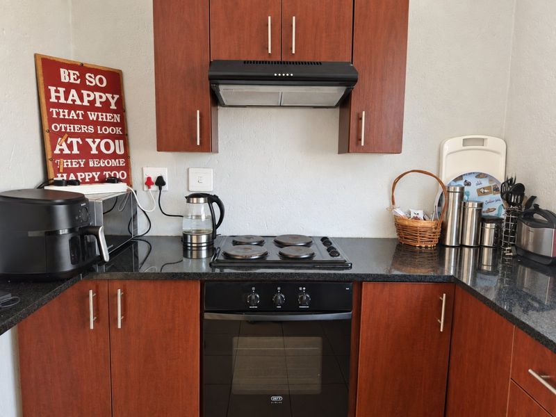 A functional kitchen featuring dark wood cabinetry, granite countertops, and integrated appliances including an electric hob, oven, and extractor fan.