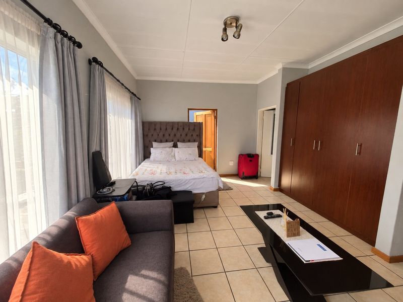 Spacious bedroom featuring large built-in wooden cupboards, tiled flooring, and natural light through floor-to-ceiling windows.