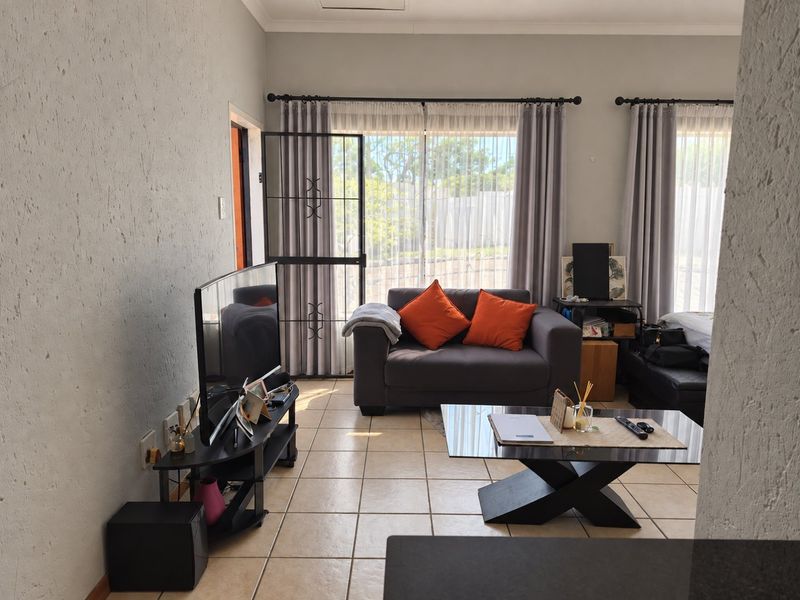 A bright living room featuring tiled flooring and large sliding glass doors with security gates, providing direct access to the outdoor area.