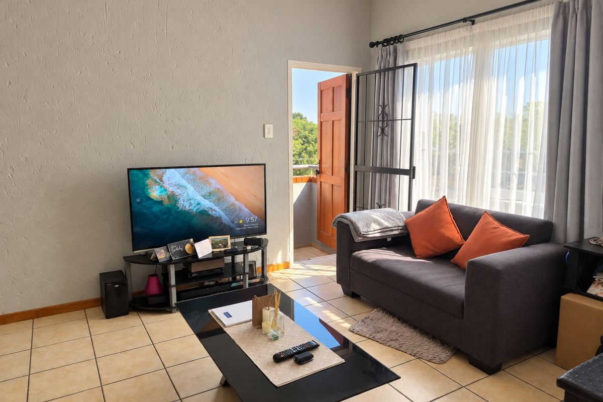 A living room featuring tiled flooring, textured walls, and direct access to an outdoor balcony through a security gate.