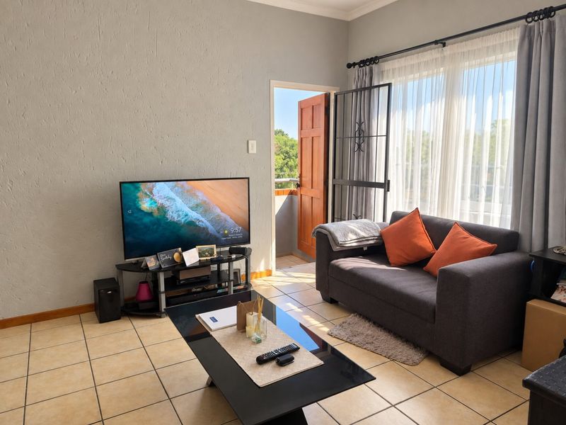 A living room featuring tiled flooring, textured walls, and direct access to an outdoor balcony through a security gate.