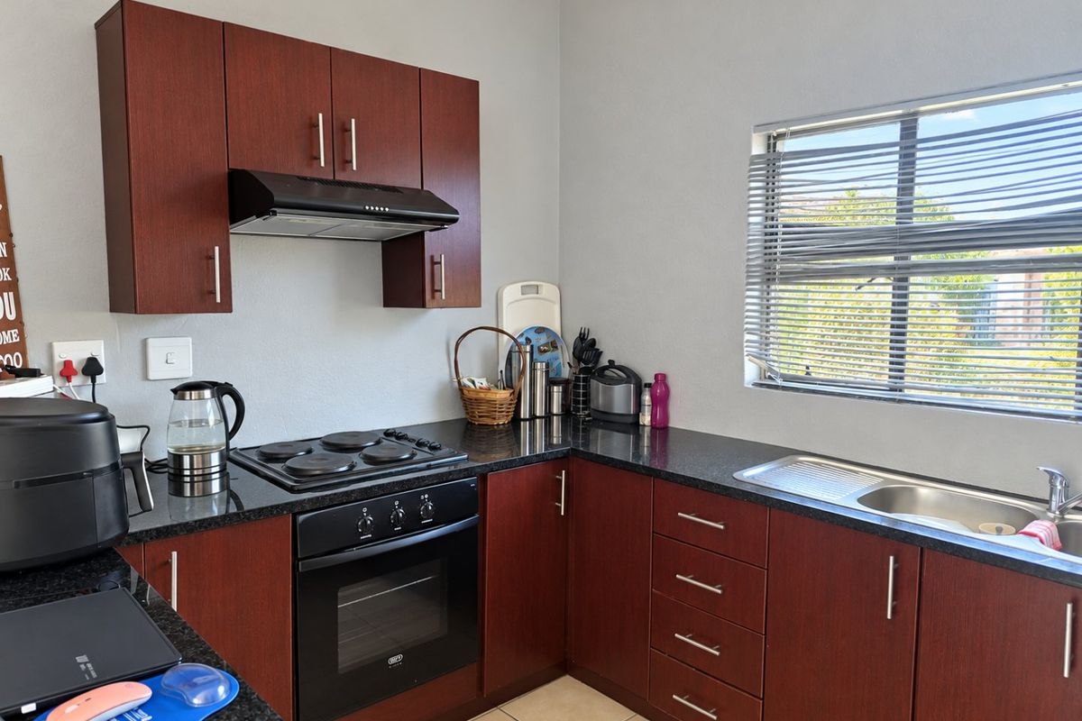 A functional kitchen featuring dark wood cabinetry, granite countertops, a built-in oven with hob, extractor fan, and a stainless steel sink.