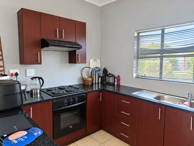 A functional kitchen featuring dark wood cabinetry, granite countertops, a built-in oven with hob, extractor fan, and a stainless steel sink.