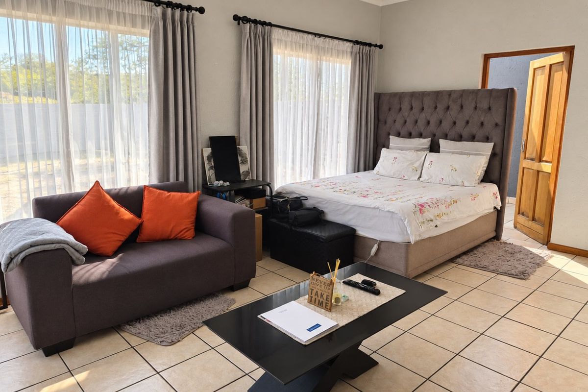 A spacious bedroom featuring tiled flooring, large windows with curtain rails, and a wooden door frame, offering a functional and well-lit living space.