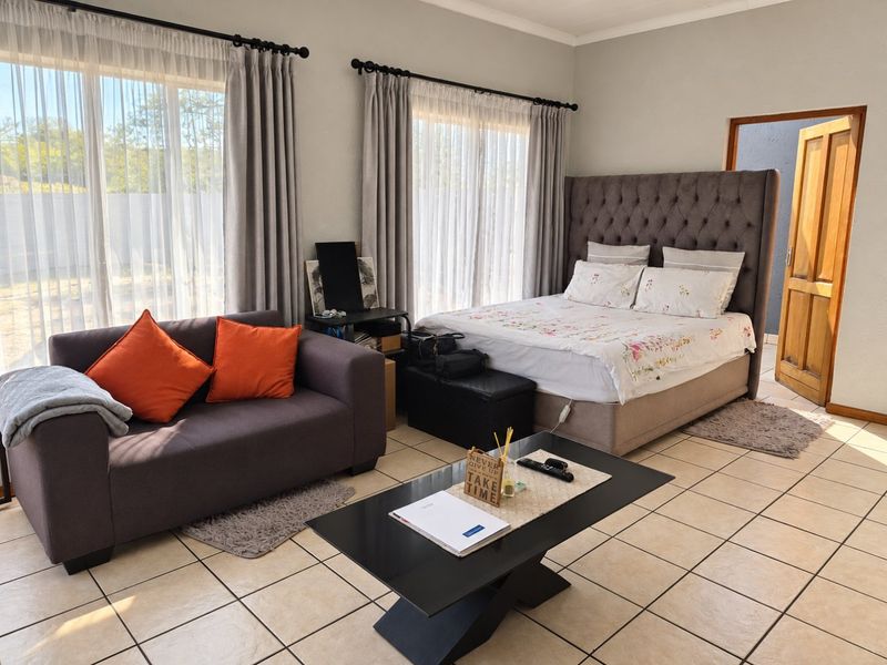 A spacious bedroom featuring tiled flooring, large windows with curtain rails, and a wooden door frame, offering a functional and well-lit living space.