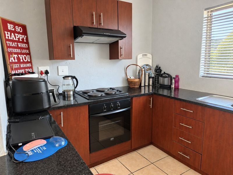 A functional kitchen featuring dark wood cabinetry, granite countertops, a built-in oven, electric hob, and an extractor fan with tiled flooring.