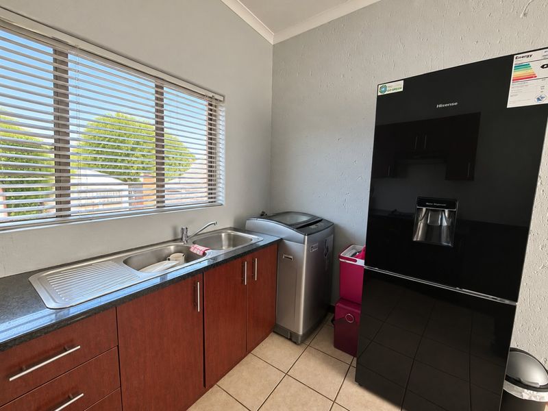 A functional laundry area featuring built-in wooden cabinetry, a double stainless steel sink with mixer tap, and tiled flooring.