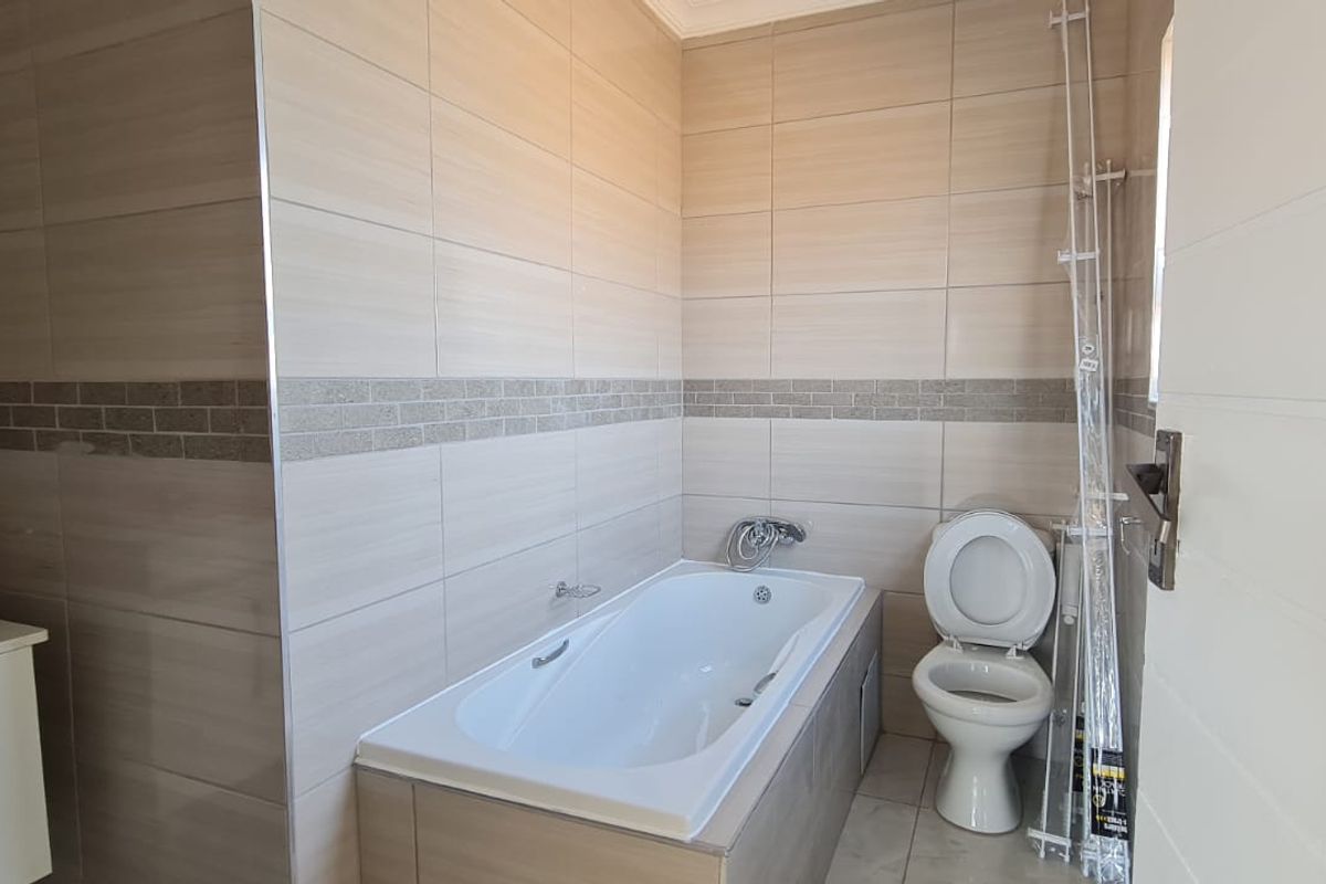 A clean, modern bathroom featuring neutral wall tiles, a built-in bathtub, a vanity with a basin, and a standard toilet.