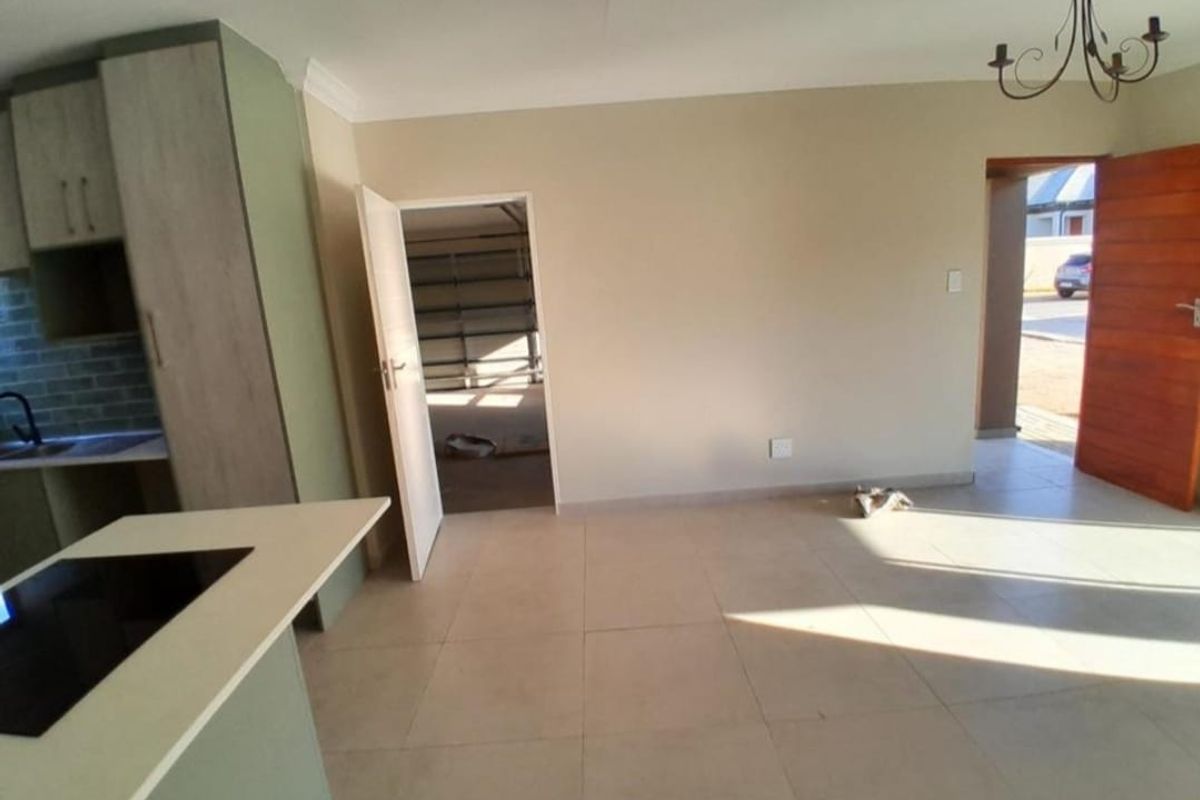 An open-plan living and kitchen area featuring modern cabinetry, a central island with a built-in hob, and neutral tiled flooring throughout.