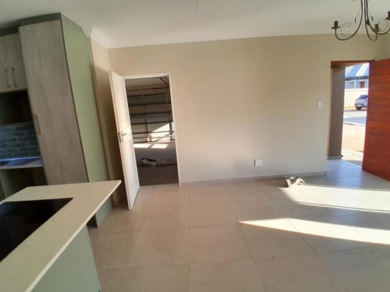 An open-plan living and kitchen area featuring modern cabinetry, a central island with a built-in hob, and neutral tiled flooring throughout.