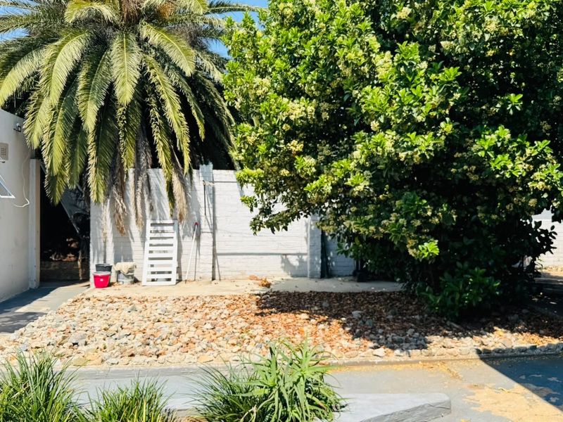 A rear exterior area featuring a paved section, a rock garden, and a boundary wall with mature landscaping.
