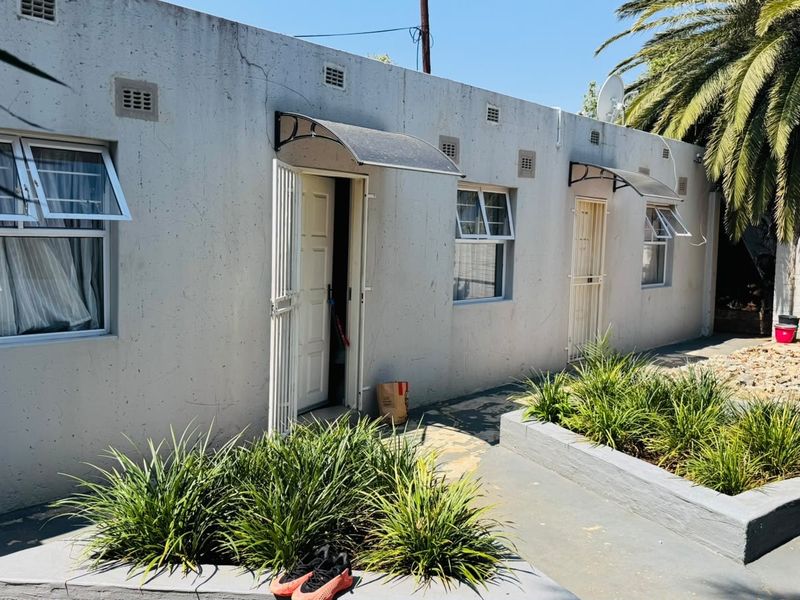 Rear exterior view of the apartment building featuring concrete paving, raised garden beds, and security gates over the entrance doors.