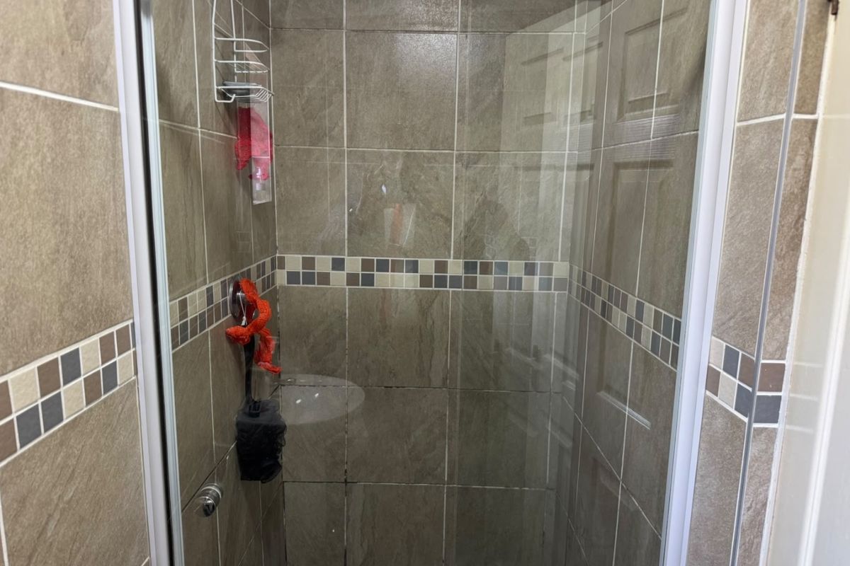 A shower stall featuring neutral-toned wall tiles with a decorative mosaic accent border and a glass enclosure.