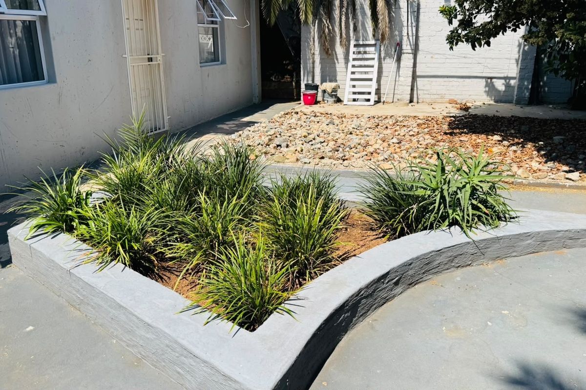 Rear exterior area featuring a raised garden bed, concrete paving, and access to the building via a security gate.