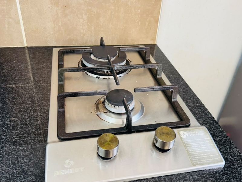 A close-up view of a two-burner gas hob set into a dark granite countertop with a neutral tiled splashback.