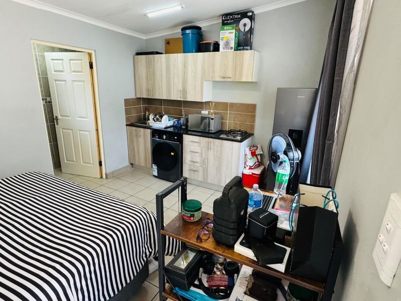 Compact open-plan studio apartment featuring a functional kitchenette with built-in cabinetry, tiled flooring, and direct access to an adjoining bathroom.