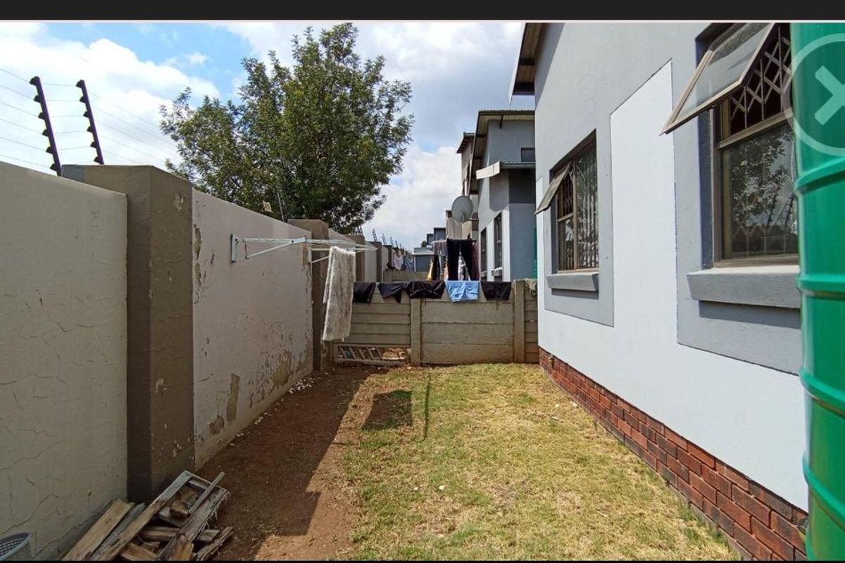 Rear exterior view of the property featuring a small garden area, perimeter wall with electric fencing, and brick-based wall construction.