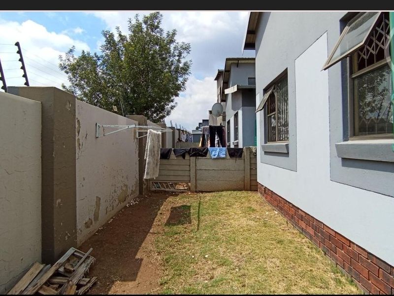 Rear exterior view of the property featuring a small garden area, perimeter wall with electric fencing, and brick-based wall construction.