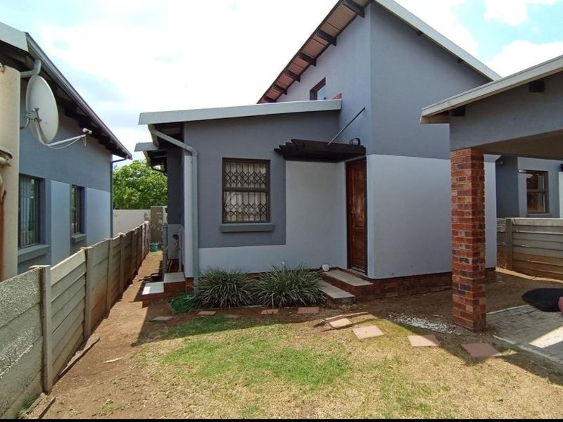 Rear view of the property featuring a small garden area, paved walkway, brick pillar, and precast concrete boundary wall.