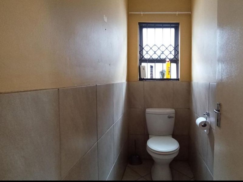 A compact bathroom featuring tiled walls, tiled flooring, and a window with security bars.