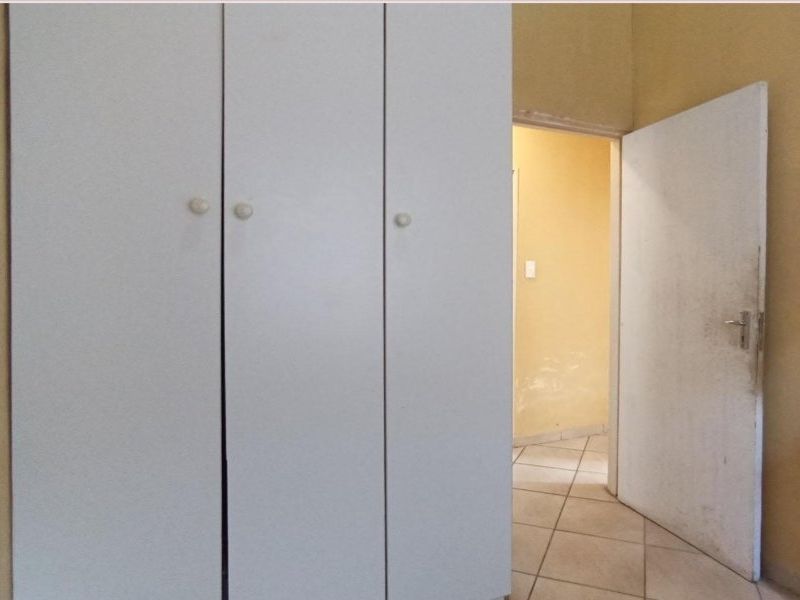 A bedroom featuring built-in cupboards and tiled flooring, showing signs of wear on the walls and door.