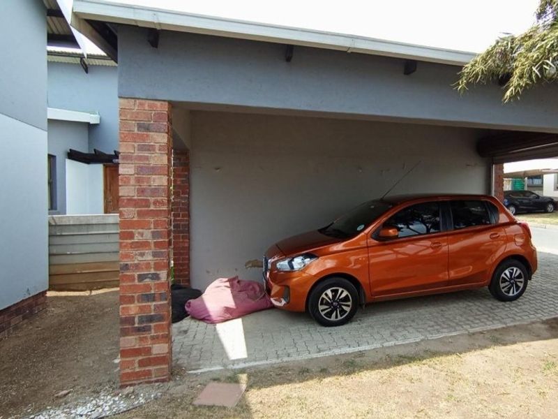 A covered carport area featuring a brick pillar support and paved flooring, providing sheltered off-street parking.