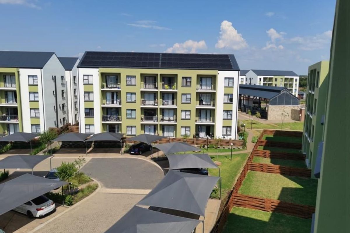 Aerial view of a modern apartment complex featuring solar panels, covered parking bays, landscaped grounds, and private balconies.