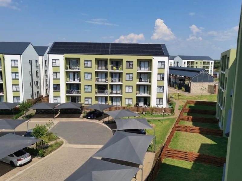 Aerial view of a modern apartment complex featuring solar panels, covered parking bays, landscaped grounds, and private balconies.