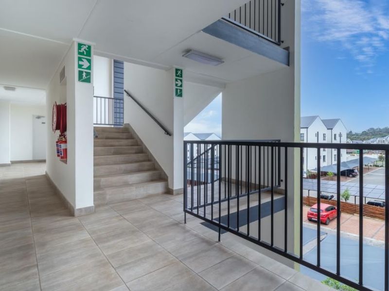 An open-air apartment complex hallway featuring tiled flooring, a staircase with metal balustrades, and essential fire safety equipment.