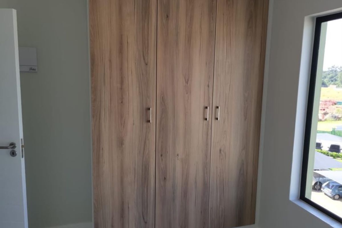 A bright bedroom featuring modern wood-finish built-in cupboards and a large window with an exterior view.