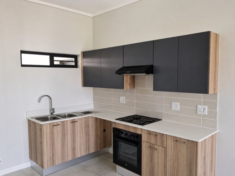 Modern kitchen featuring wood-grain cabinetry, stone countertops, a double sink, and integrated appliances including an oven, hob, and extractor fan.