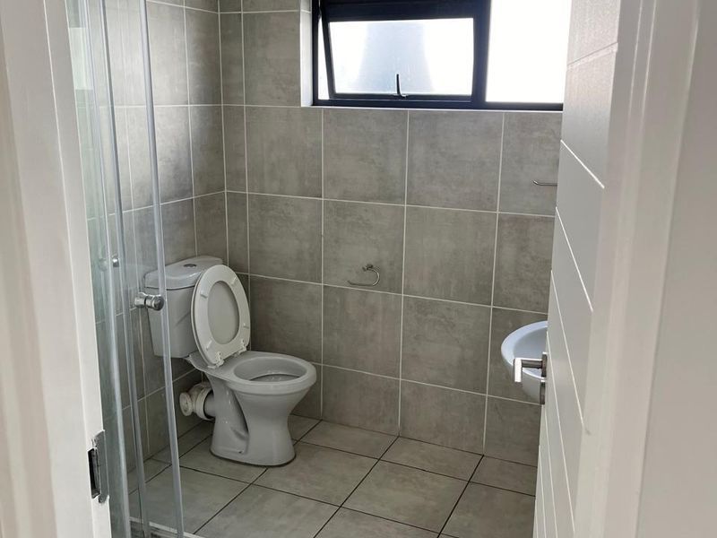 A compact bathroom featuring neutral wall and floor tiles, a glass shower enclosure, a standard toilet, and a wall-mounted basin.