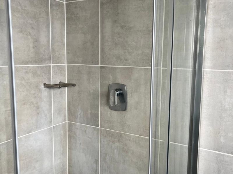 A clean, modern shower stall featuring grey ceramic wall tiles, a glass enclosure, and chrome fixtures.