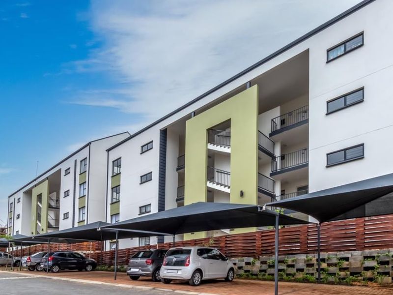 Modern apartment complex exterior featuring covered parking bays, a retaining wall, and multi-level balconies with contemporary architectural design.