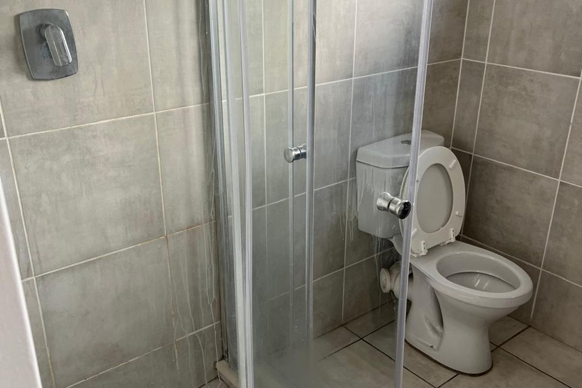 A functional bathroom featuring a glass shower enclosure, toilet, and neutral floor-to-ceiling tiling throughout.